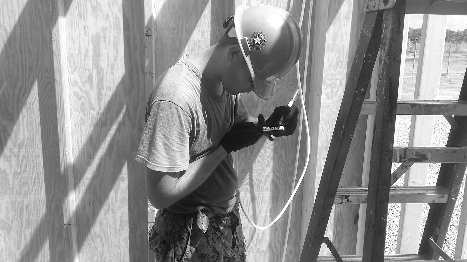 An electrician in a hard hat marking a cable run on a timber-framed wall